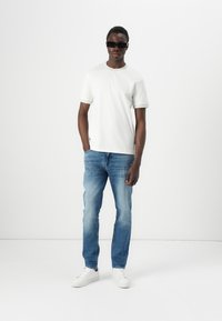 Camiseta blanca de manga corta, jeans de mezclilla azul y zapatillas blancas. Unas gafas de sol rectangulares negras añaden contraste al conjunto. Estilo simple y casual.