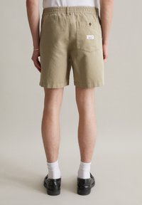 Khaki shorts with an elastic waistband, textured cotton fabric, and a rear pocket featuring a label. Worn with white socks and black shoes.
