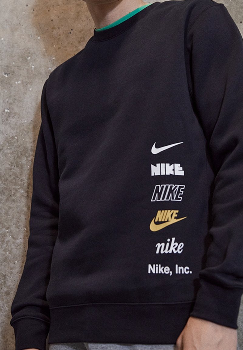 Persona con sudadera negra que presenta seis logotipos de Nike diferentes y texto en blanco, negro y dorado en el lado izquierdo.
