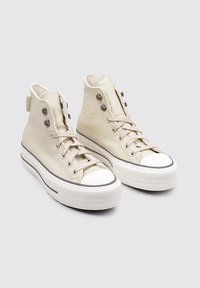 Zapatillas altas de cuero beige con un acabado texturizado, puntera redonda, suela de goma blanca, ojales para los cordones y un logo en el lateral.