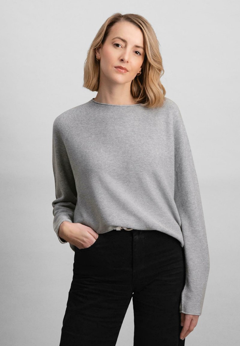Maglione grigio chiaro a maniche lunghe con scollatura a girocollo, dalla texture morbida e dal fit rilassato, abbinato a pantaloni neri a vita alta.