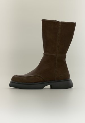 Botte en daim brun foncé mi-mollet avec semelle noire, bout arrondi, coutures visibles et fermeture éclair latérale sur fond neutre.