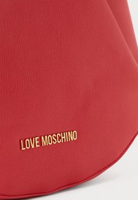 Mala de mão em pele sintética vermelha com uma textura suave, forma arredondada e um logo em tom dourado "LOVE MOSCHINO".