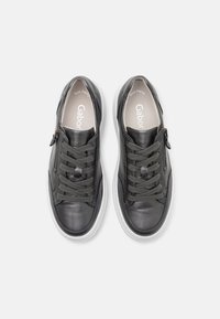 Paire de baskets en cuir noir avec semelles blanches, lacets et fermetures éclair latérales, vues de dessus sur fond blanc.