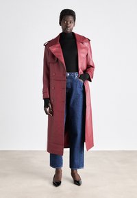 Rød lædertrenchcoat med bred krave og dobbeltknaplukning, parret med en sort turtleneck og højtaljede denim jeans. Sorte hæle.