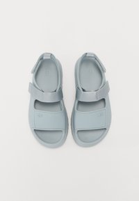 Lys blå sandaler laget av syntetisk materiale, med lukket tå, justerbar stropp og teksturert fotseng med merkevarelogo.