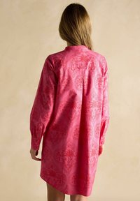 Rosa Langarmhemdkleid mit strukturiertem Blumenmuster, Knopfmanschetten und einem leicht gebogenen Saum. Rückansicht mit Kragen.