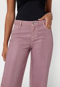 Ružové denimové nohavice s perforovaným dizajnom. Majú klasický päť-vreckový štýl, zapínanie na gombík a strieborné akcenty. Voľný strih.
