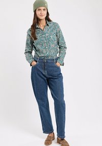 Grünes, floral gemustertes Hemd mit langen Ärmeln, kombiniert mit high-waisted blauen Jeanshosen und braunen Slip-On Schuhen mit Leopardenmuster.