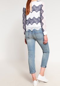 Top in pizzo con un motivo ondulato blu navy e bianco, con schiena a oblò, abbinato a jeans azzurri arrotolati e sneakers bianche.