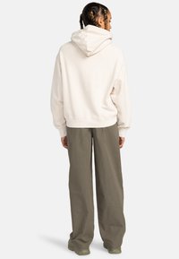 Light beige hooded sweatshirt with a relaxed fit, featuring ribbed cuffs and hem. Paired with loose olive-green pants.