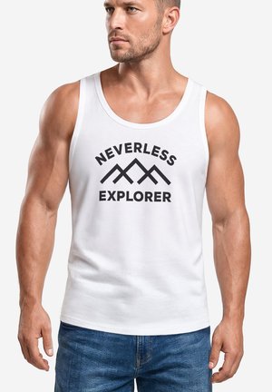 Muskelbepackter Mann trägt ein weißes Tanktop mit dem Text "NEVERLESS EXPLORER" und einem Bergmotiv, kombiniert mit blauen Jeans, vor einem schlichten Hintergrund.
