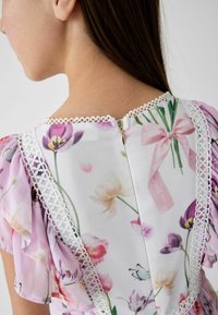 Blumenkleid mit einem weißen Spitzenbesatz entlang des Halsausschnitts und der Ärmel, mit einem Reißverschluss am Rücken. Lila und rosa Blumenmuster über das gesamte Kleid.
