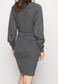 Grau geripptes Strickkleid mit langen Ärmeln und figurbetonter Silhouette, mit definierter Taille und weichem Material, geeignet für legere Anlässe.