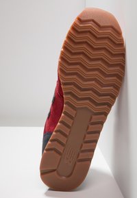 Sole červeného a černého tenisky s hlubokým cik-cak vzorem a hnědou gumovou přilnavostí, postavená vzpřímeně na bílé ploše.