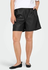 Crne kratke hlače od umjetne kože s glatkom teksturom, s bočnim džepovima i opuštenim krojem, u kombinaciji s jednostavnim crnim balerinkama.