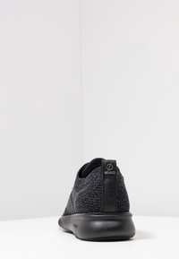 Sneaker nera con una toma superiore in maglia texturizzata e suola in gomma nera liscia. Accentuata da un logo nero sul tallone e un design a profilo basso.