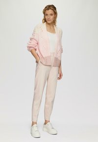 Różowy ombre sweter z dzianiny z otwartym przodem, luźnymi rękawami, w połączeniu z jasnoróżowymi spodniami i białymi sneakerami na grubej podeszwie. Gładka tekstura, luźny fason.