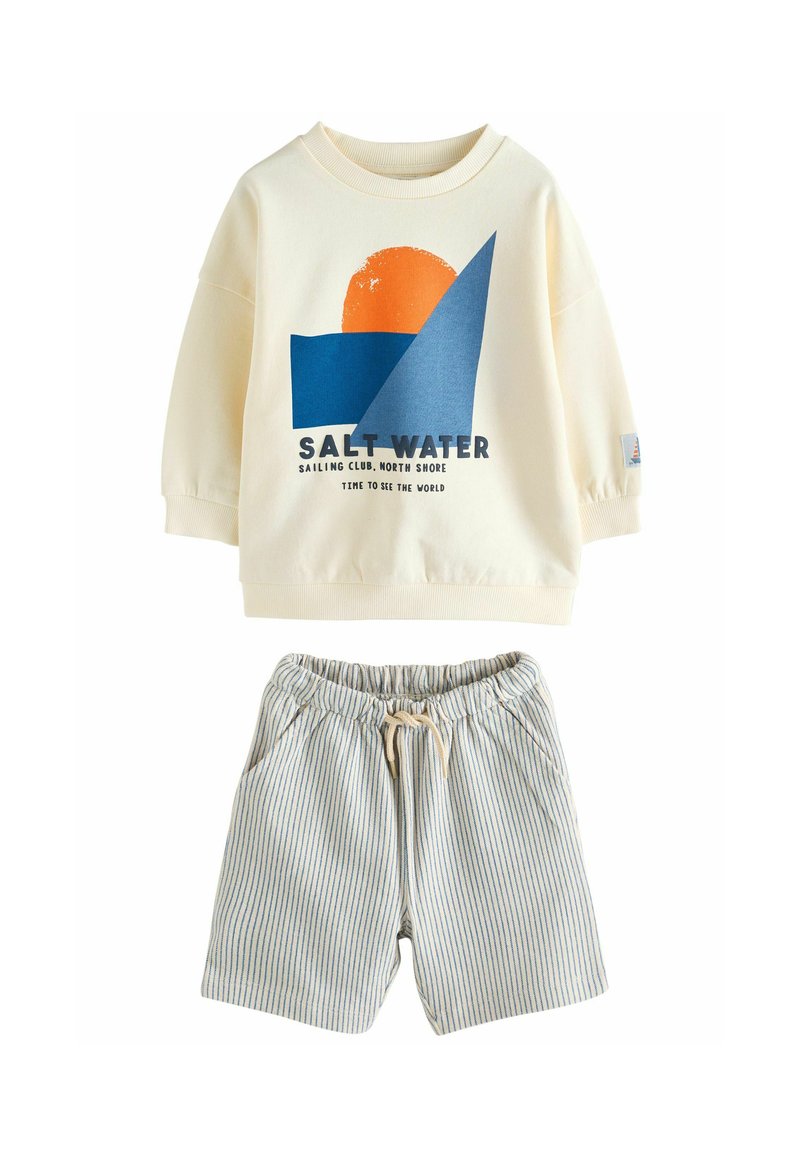 Sweatshirt clair avec un design graphique bleu et orange, associé à un short rayé avec une taille élastique et un cordon de serrage.