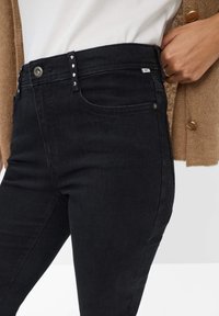 Jeans in denim nero con un design aderente, vita alta, chiusura con bottone e passanti per cintura, caratterizzati da borchie argentate sulle tasche anteriori.