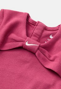 Rebrastani roza bluzica z detajlami v obliki pentlje na vratu in belim logotipom Nike. Mehka tekstura z zaobljenim ovratnikom. Velikosti 6-12 so vidne na označevalni etiketi.