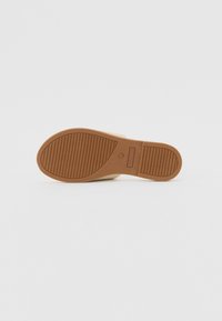 Semelle en caoutchouc d’une chaussure beige sans lacets avec motif de bande de roulement texturé, montrée à plat sur fond blanc.