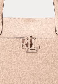 Vaaleanpunainen nahkainen kassi, jossa on teksturoidun pinnan lisäksi erottuva leikattu RL-logo-yleiskuva, ommeltu etupaneeliin.