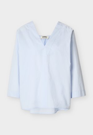 Svetlo modra bluza z dolgimi rokavi, z globokim V-izrezom in sproščenim krojem, prikazana na belem ozadju.