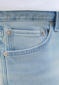 Un tessuto in denim azzurro chiaro mette in mostra una tasca frontale con rivetti argentati e cuciture in vista, riflettendo un design casual e ben realizzato.