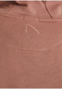 Růžová bavlněná mikina s hladkou strukturou, která má jemně vyšívaný detail ve tvaru trojúhelníku na zadní straně.