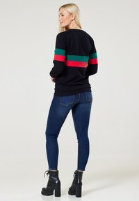 Schwarzes longsleeve Oberteil mit roten und grünen horizontalen Streifen, kombiniert mit eng anliegenden blauen Jeans und schwarzen Plateaustiefeln.