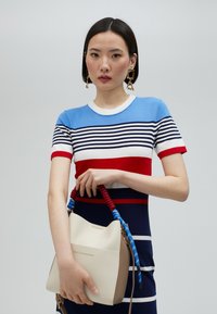 Randig stickad topp i blått, vitt och rött med korta ärmar, kombinerad med en beige bucket-väska med ett vävt handtag i rött och blått.