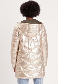 Manteau rembourré beige clair avec une finition brillante, doté d'une capuche, d'un motif matelassé en losanges et d'une doublure vert olive.
