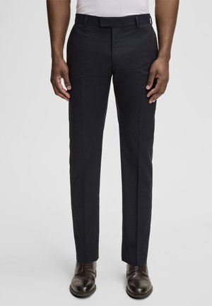 Donkerblauwe broek met een getailleerde pasvorm, een soepele textuur, riemlussen en zijzakken, gecombineerd met bruine nette schoenen.