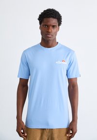 Light blue crew-neck t-shirt with short sleeves, featuring a white "ellesse" logo and a colorful accent graphic on the left chest.