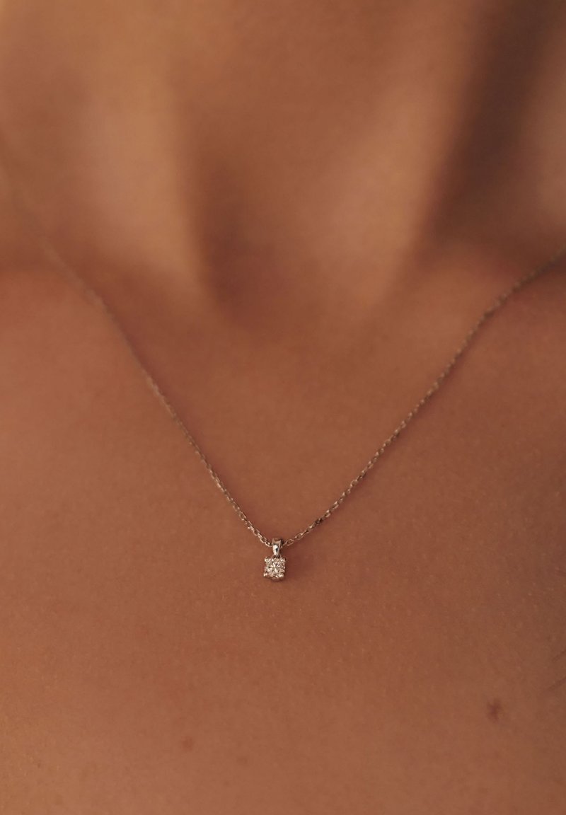 Collier en argent avec une chaîne délicate ; présente un petit pendentif carré avec une pierre claire et scintillante au centre.