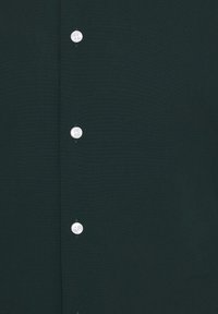 Ciemnozielony materiał z pionowym rzędem czterech białych guzików przyszytych dopasowaną zieloną nicią.