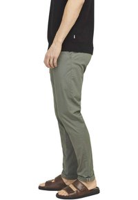 Pantalons khaki au design slim fit, fabriqués à partir d'un tissu léger ; portés avec des sandales en cuir marron, dotées d'une sangle réglable.