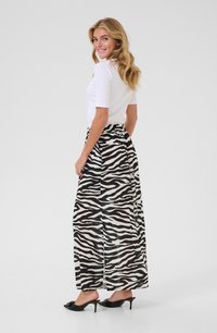 Jupe maxi à rayures zèbre noir et blanc avec une taille élastique, associée à un haut ajusté blanc à manches courtes et des talons noirs ouverts.