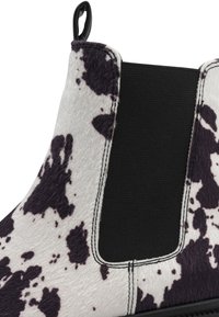 Bottines Chelsea en cuir de vache noir et blanc, dotées d'un panneau latéral élastique en tissu, d'une texture lisse et de détails de couture contrastés.