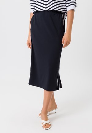 Donkerblauwe midi-rok gemaakt van zachte stof met een aansluitende taille, voorzien van witte zijstrepen en een licht uitlopende zoom. Gecombineerd met witte sandalen.