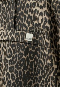 Leopardprint-stof i nuancer af beige og sort med en struktureret finish. Indeholder en synlig hvid label med teksten "SOFIE SCHNOOR".