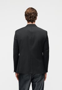 Μαύρο σακάκι με εφαρμοστή γραμμή, γιακάδες με σχισμή και μονό πίσω άνοιγμα, σε συνδυασμό με σκούρο τζιν. Λείο υλικό και δομημένος σχεδιασμός.