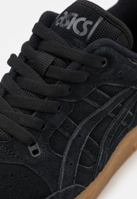 Černé semišové boty na volný čas s texturovaným povrchem, obsahující černé šňůrky, prodyšný jazyk a gumovou podrážku. Logo Asics na jazyku.