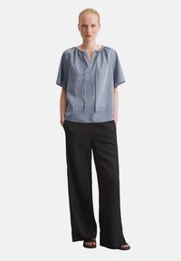 Camicia a maniche corte celeste con scollo a v e dettagli con coulisse, abbinata a pantaloni neri a gamba larga e sandali bassi.
