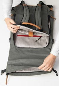 Grau Rucksack mit gepolsterten Trägern, einem Lederakzent und einem Reißverschluss, der ein kariertes Innenfutter und eine rote Reißverschlusstasche enthüllt.