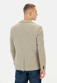 Beige strukturierter Blazer mit Reverskragen, einfacher Rückenbelüftung und Dreiknopfbündchen, kombiniert mit blauen Jeans.