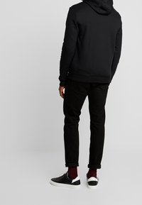 Svart hoodie med justerbara dragsko, kombinerad med svarta jeans och svarta sneakers med vita detaljer och uppvikta muddar.