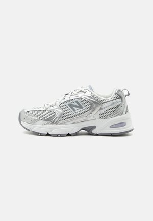 Weißer und grauer New Balance 530 Sportschuh mit Mesh-Einsätzen und gepolsterter Sohle vor einfachem Hintergrund.