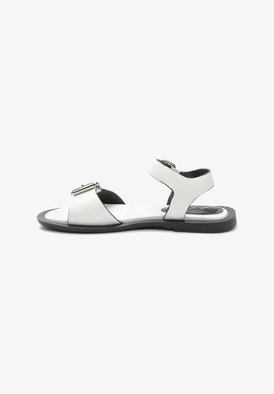 Weiße Ledersandalen mit einem Kreuzriemendesign, verstellbarem Knöchelriemen und einer schwarzen Gummisohle. Schnallenverzierung an der Vorderseite.